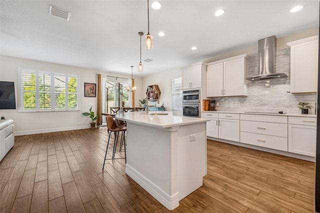 4808 Jackson Club Loop, Tampa, FL 33624 - kitchen featuring wall chimney range hood, stainless steel double oven, light wood finished floors, black electric cooktop, and light countertops