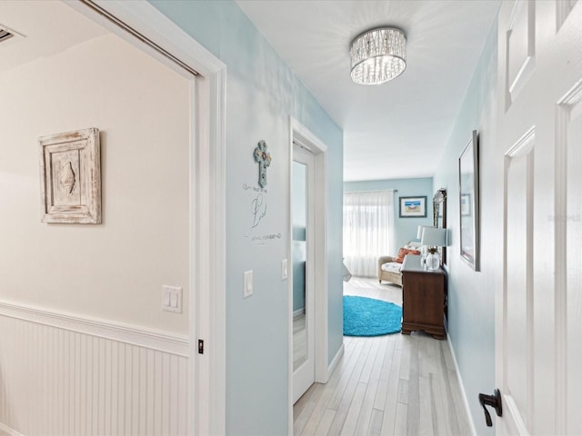 corridor featuring light wood finished floors and a chandelier