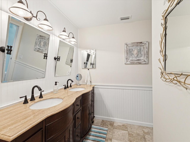 full bath with double vanity, visible vents, wainscoting, and a sink