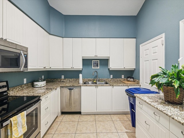 kitchen featuring light stone countertops, appliances with stainless steel finishes, a sink, white cabinetry, and light tile patterned floors