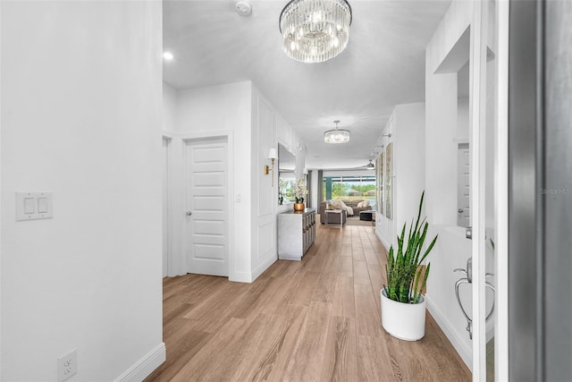 corridor with baseboards, a notable chandelier, and light wood-style flooring