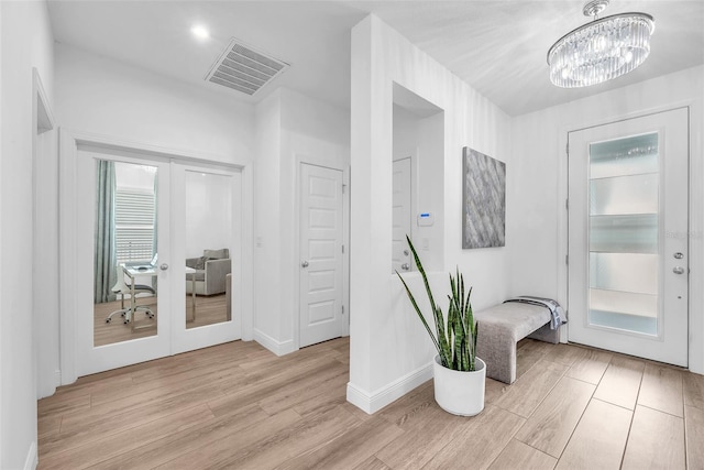 interior space with light wood-style floors, a notable chandelier, french doors, and visible vents