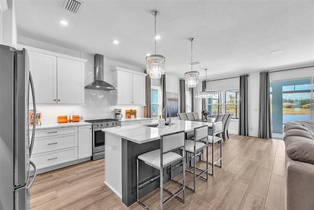 kitchen with visible vents, light wood-type flooring, wall chimney exhaust hood, a sink, and appliances with stainless steel finishes