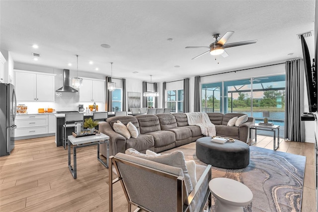 living room featuring a ceiling fan, a textured ceiling, visible vents, and light wood-type flooring