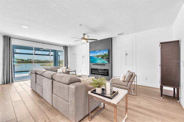 living room featuring visible vents, baseboards, ceiling fan, a textured ceiling, and light wood-style flooring