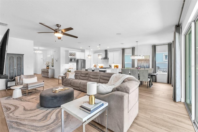 living room featuring light wood finished floors and ceiling fan with notable chandelier