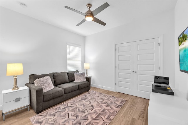 living room featuring a ceiling fan, baseboards, and light wood-type flooring
