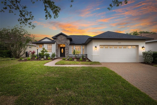 view of front of home with an attached garage, stone siding, stucco siding, a front yard, and decorative driveway