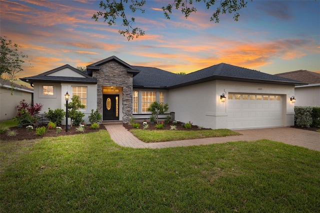 view of front of house with an attached garage, stone siding, stucco siding, a front yard, and decorative driveway
