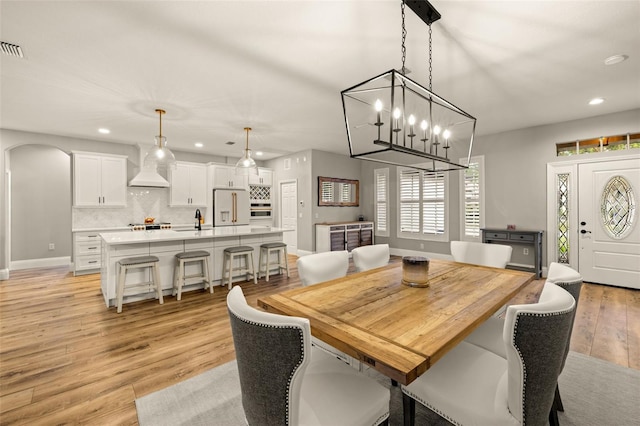dining space with light wood-style floors, arched walkways, a chandelier, recessed lighting, and baseboards