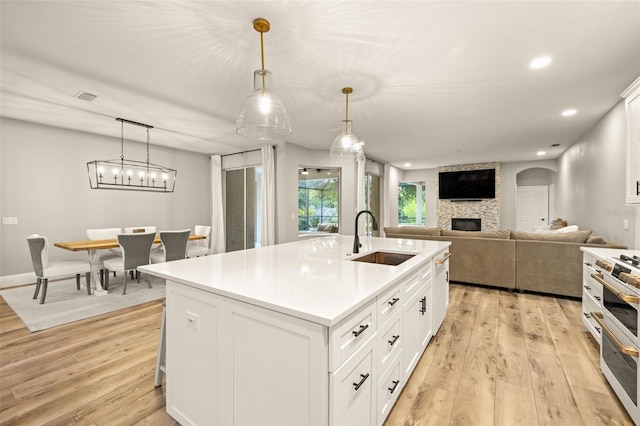 kitchen featuring a fireplace, a sink, light countertops, light wood-style floors, and an island with sink