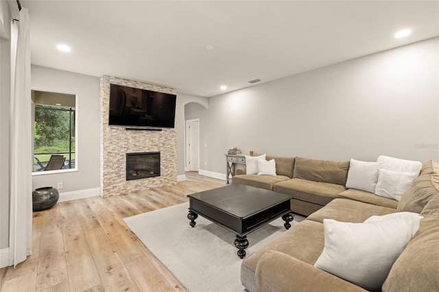 living area featuring baseboards, a stone fireplace, arched walkways, and light wood-style flooring