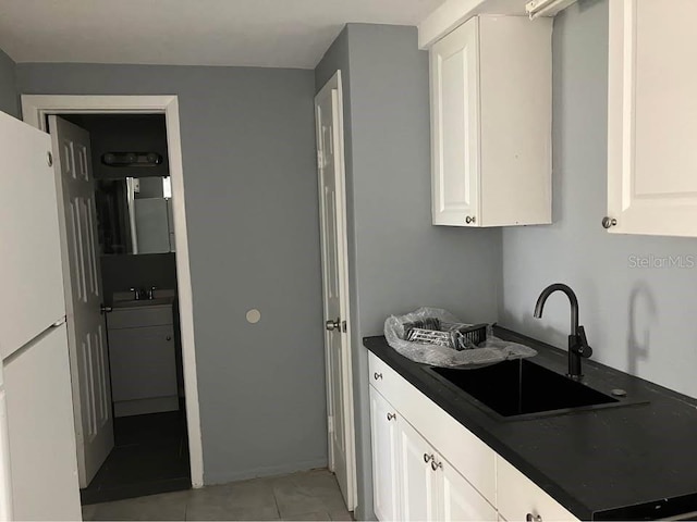 kitchen featuring freestanding refrigerator, dark countertops, a sink, and white cabinets