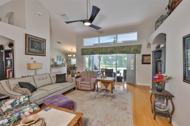 living area featuring wood finished floors, baseboards, ceiling fan with notable chandelier, and a high ceiling