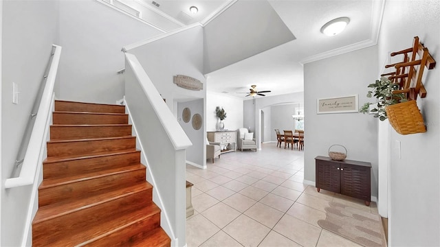 stairway featuring crown molding, ceiling fan, arched walkways, tile patterned floors, and baseboards