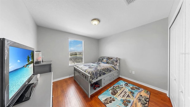 bedroom with visible vents, baseboards, wood finished floors, and a closet