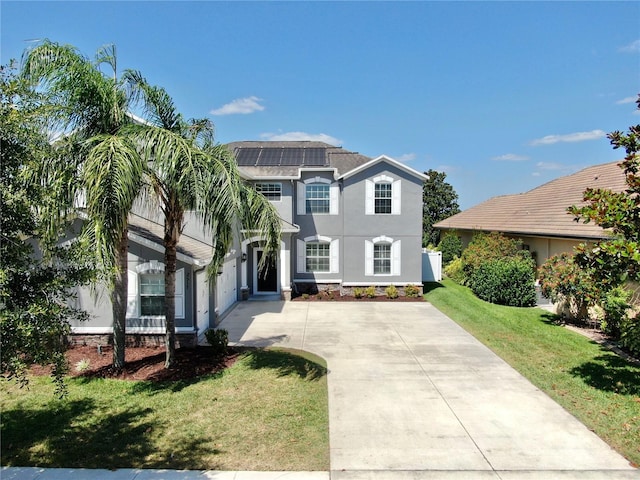 view of front of house featuring stucco siding, concrete driveway, roof mounted solar panels, and a front lawn