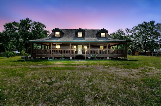 back of house at dusk featuring a yard, roof with shingles, and covered porch