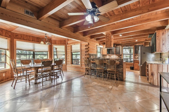 dining room with wood walls, beam ceiling, light tile patterned flooring, and wood ceiling