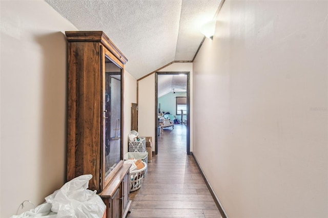 hall with lofted ceiling, hardwood / wood-style floors, a textured ceiling, and baseboards