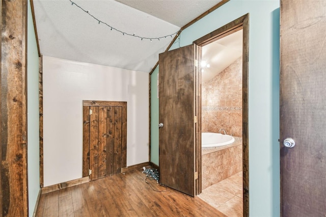 bathroom featuring hardwood / wood-style floors, tiled bath, a textured ceiling, baseboards, and vaulted ceiling