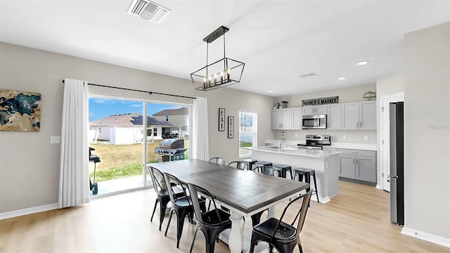 dining space with baseboards, a notable chandelier, light wood-style flooring, and visible vents