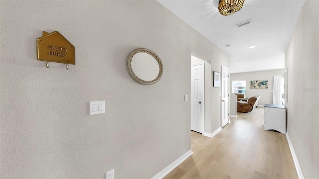 hallway with light wood-style floors, baseboards, and visible vents