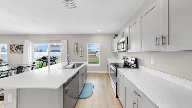 kitchen with appliances with stainless steel finishes, a center island with sink, a sink, light countertops, and light wood-style flooring