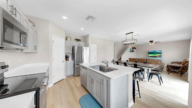 kitchen with ceiling fan, a kitchen bar, a sink, light wood-style flooring, and appliances with stainless steel finishes