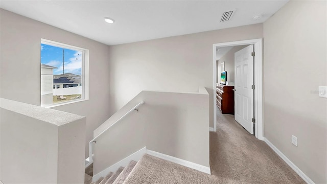 hall featuring carpet flooring, baseboards, visible vents, and an upstairs landing