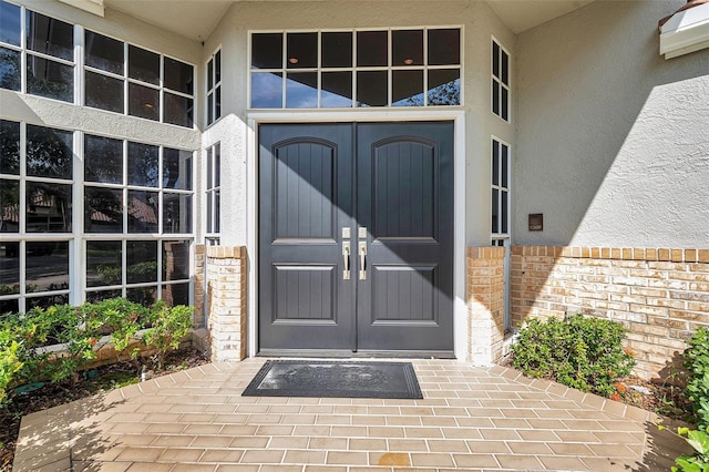 entrance to property with french doors, stucco siding, and brick siding