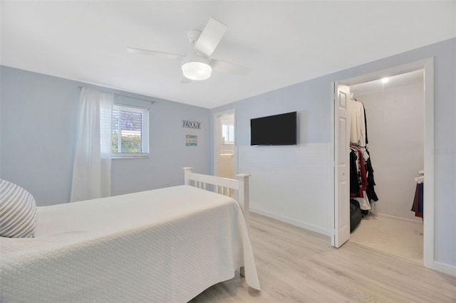 bedroom featuring a walk in closet, ceiling fan, baseboards, a closet, and light wood-style flooring