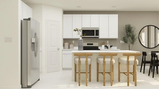 kitchen featuring appliances with stainless steel finishes, light countertops, white cabinetry, a kitchen bar, and a center island with sink