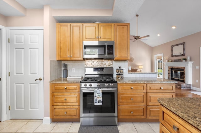 2512 Rustic Oaks Dr, Lutz, FL 33559 - kitchen with appliances with stainless steel finishes, a ceiling fan, decorative backsplash, light tile patterned floors, and a brick fireplace