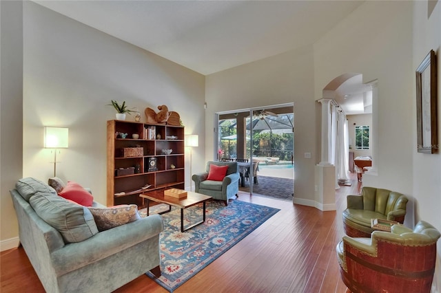 sitting room featuring arched walkways, baseboards, decorative columns, and wood finished floors