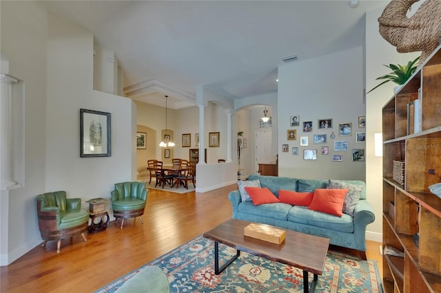 living area with arched walkways, a chandelier, wood finished floors, ornate columns, and visible vents