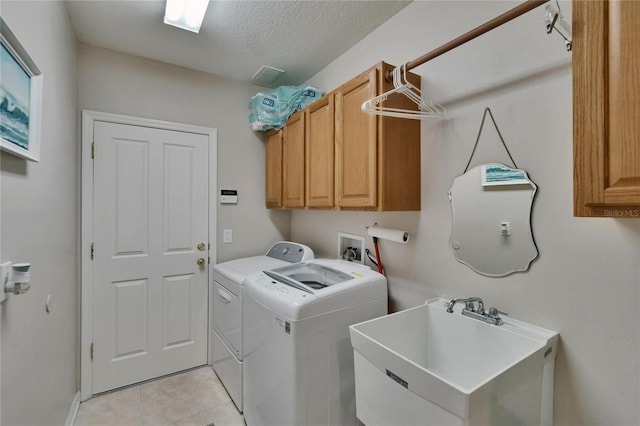 washroom with a textured ceiling, cabinet space, a sink, light tile patterned floors, and washer and clothes dryer