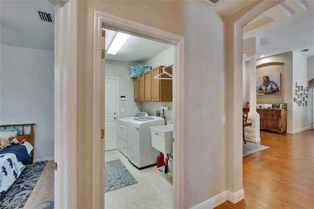 washroom with cabinet space, arched walkways, baseboards, visible vents, and washing machine and dryer