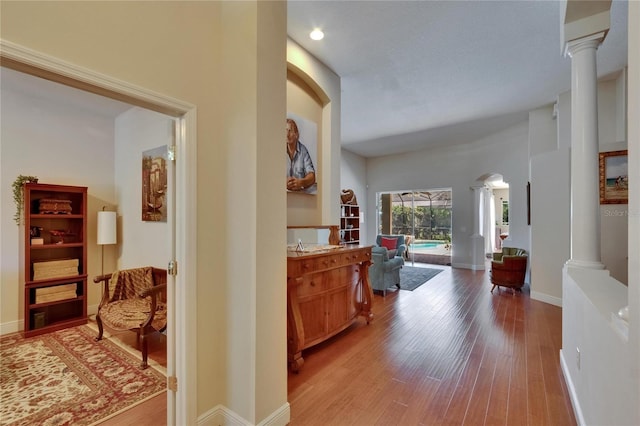 corridor with ornate columns, baseboards, arched walkways, and light wood-style floors