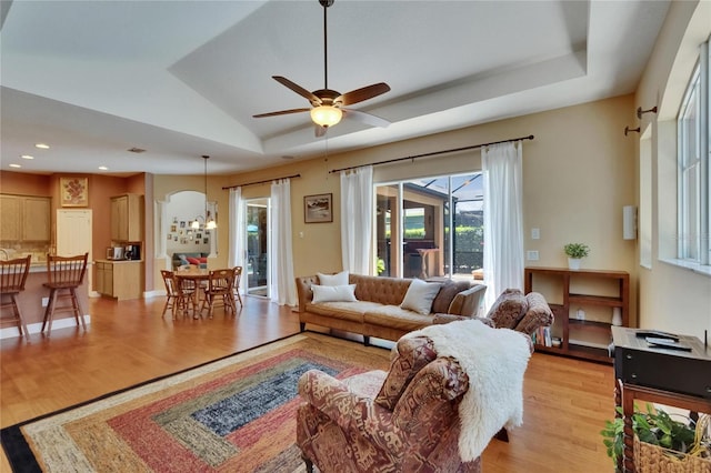 living room with ceiling fan with notable chandelier, recessed lighting, a tray ceiling, and light wood finished floors