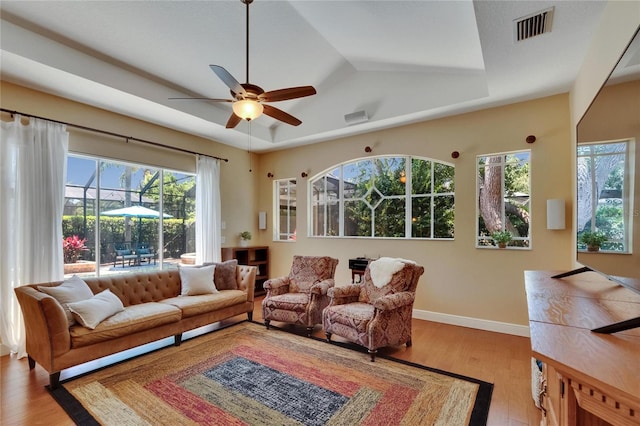 living area with a ceiling fan, a tray ceiling, visible vents, and plenty of natural light