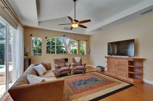 living area with baseboards, visible vents, wood finished floors, and a raised ceiling
