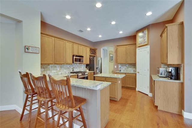 kitchen with arched walkways, appliances with stainless steel finishes, a peninsula, and tasteful backsplash