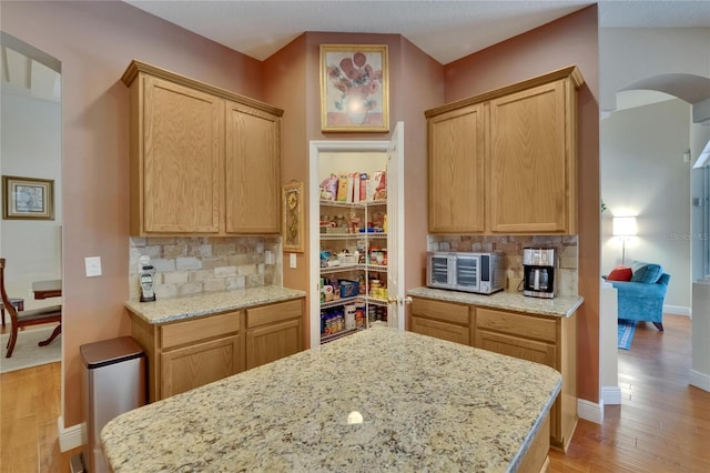 kitchen with arched walkways, a toaster, light wood-type flooring, and tasteful backsplash