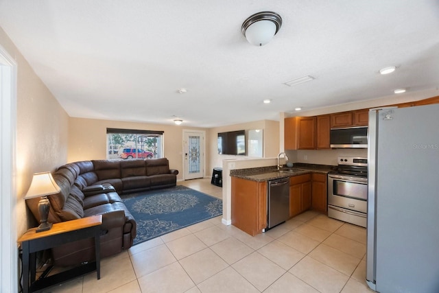 kitchen featuring a peninsula, open floor plan, brown cabinets, appliances with stainless steel finishes, and light tile patterned floors