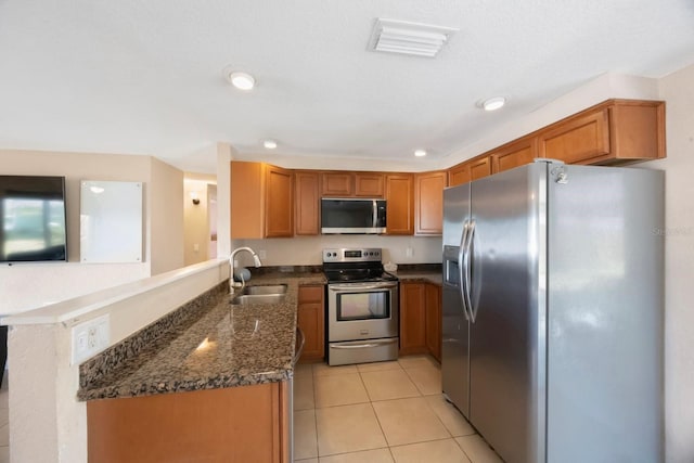 kitchen featuring brown cabinets, a sink, dark stone countertops, stainless steel appliances, and light tile patterned floors