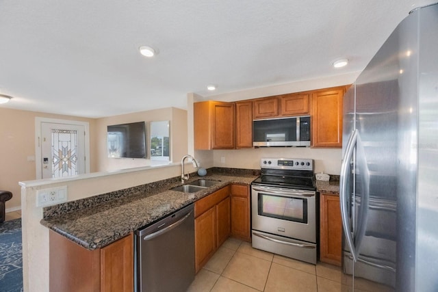 kitchen featuring brown cabinetry, a peninsula, dark stone counters, a sink, and appliances with stainless steel finishes