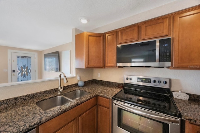 kitchen with a sink, dark stone countertops, appliances with stainless steel finishes, and brown cabinets