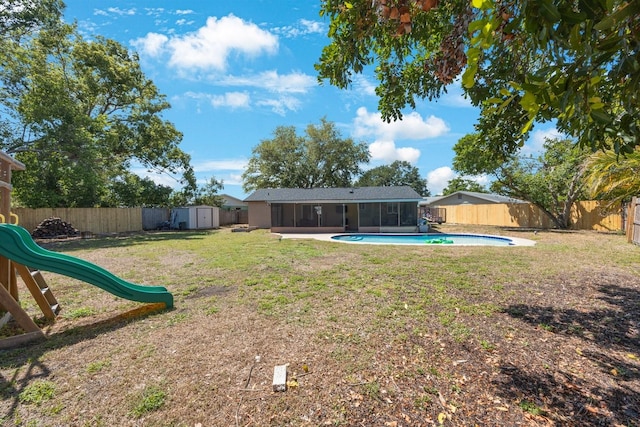 view of yard with an outdoor structure, a fenced backyard, a sunroom, and a storage unit
