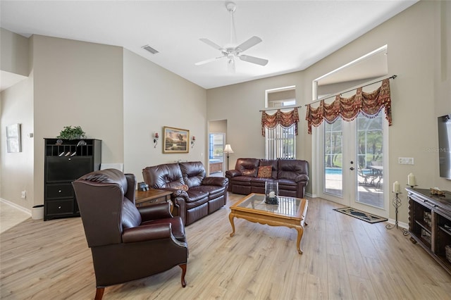 living room featuring visible vents, a towering ceiling, light wood-style floors, baseboards, and ceiling fan